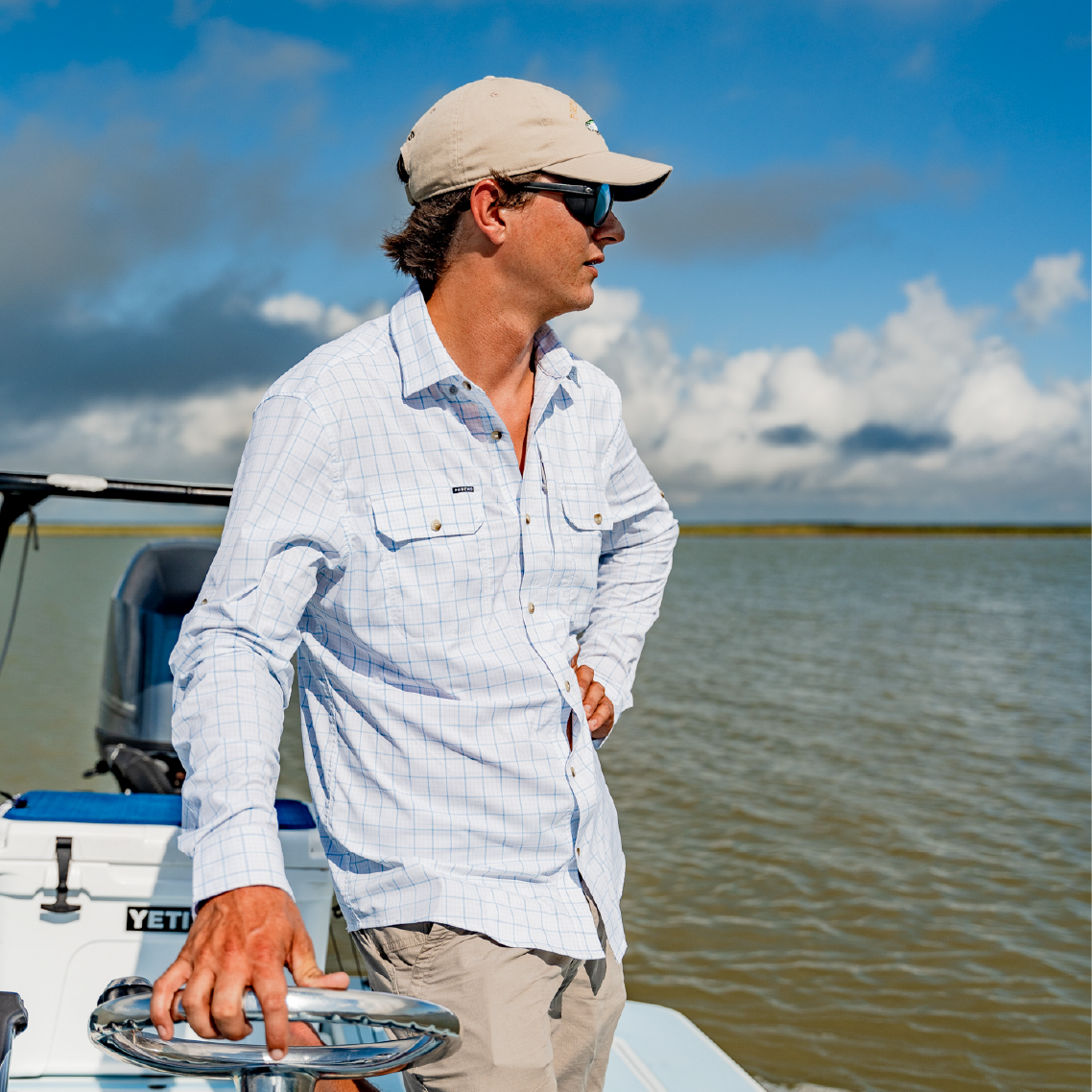 man driving a boat wearing a white long sleeve button down fishing shirt