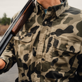 Man holding shotgun wearing camo button down shirt