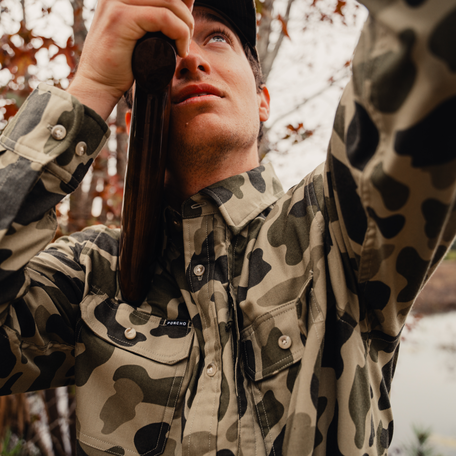 Man shooting shotgun wearing camo button down shirt