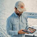 Man looking in fly box while wearing a long sleeve button up fishing shirt on a boat