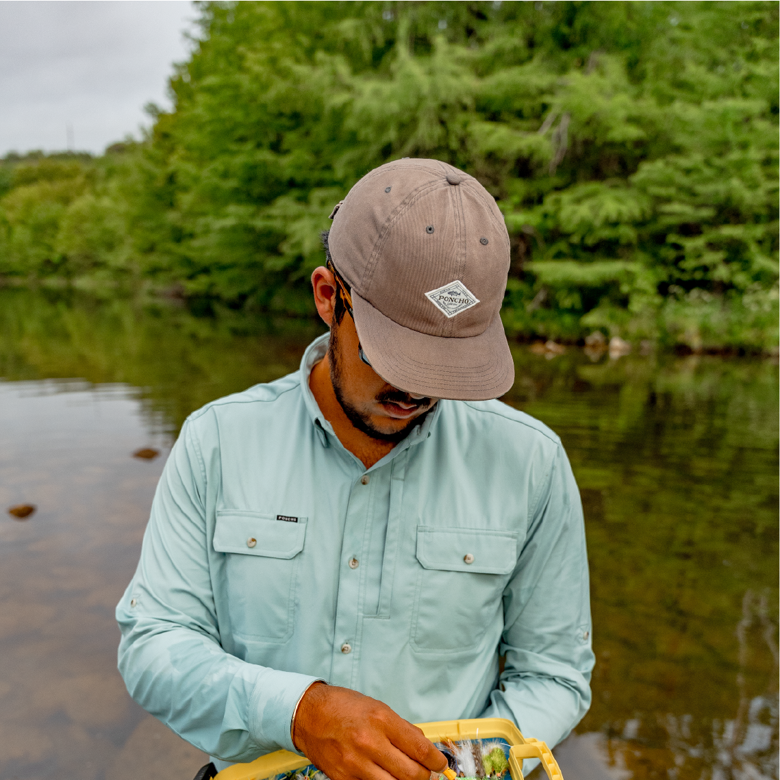 man wearing grey hat reaching into a fly box