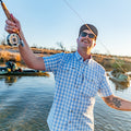 Man casting a a fly rod wearing a blue button down shirt