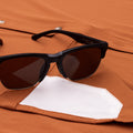 Close up of sunglasses on burnt orange shirt with lens cloth