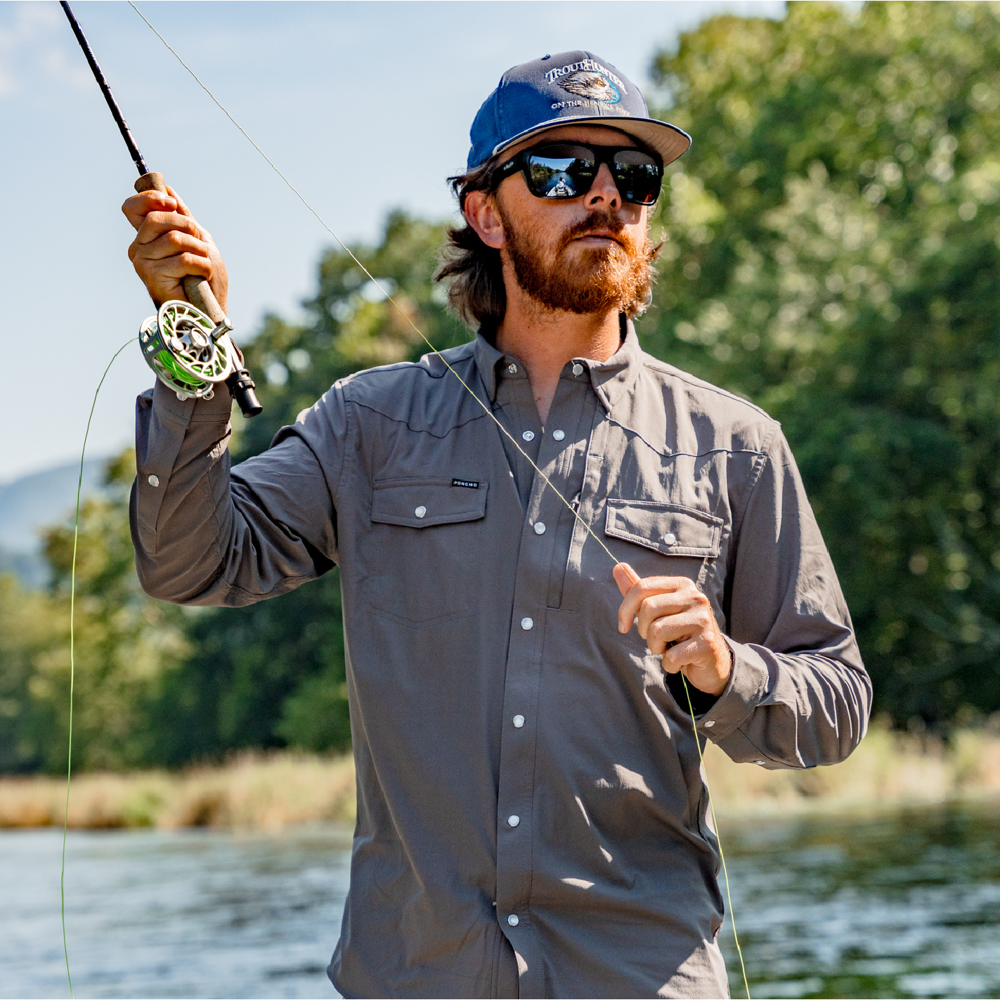 man casting a fly rod on a river in dark grey long sleeve shirt