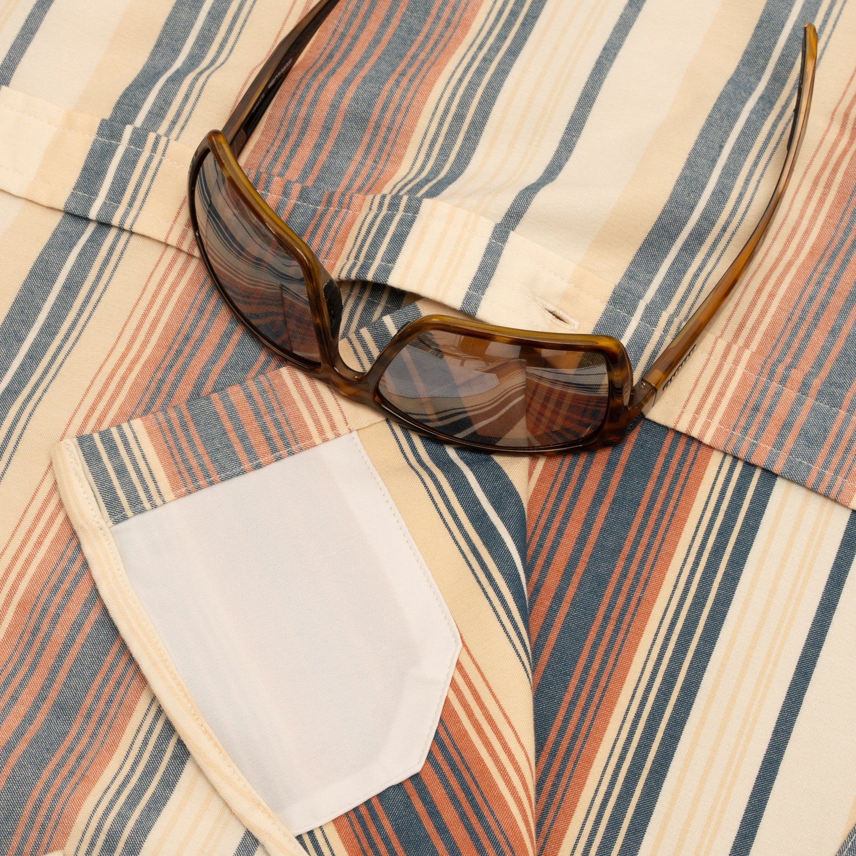 Sunglasses laying on orange and yellow striped flannel shirt with hidden sunglass cleaner fabric