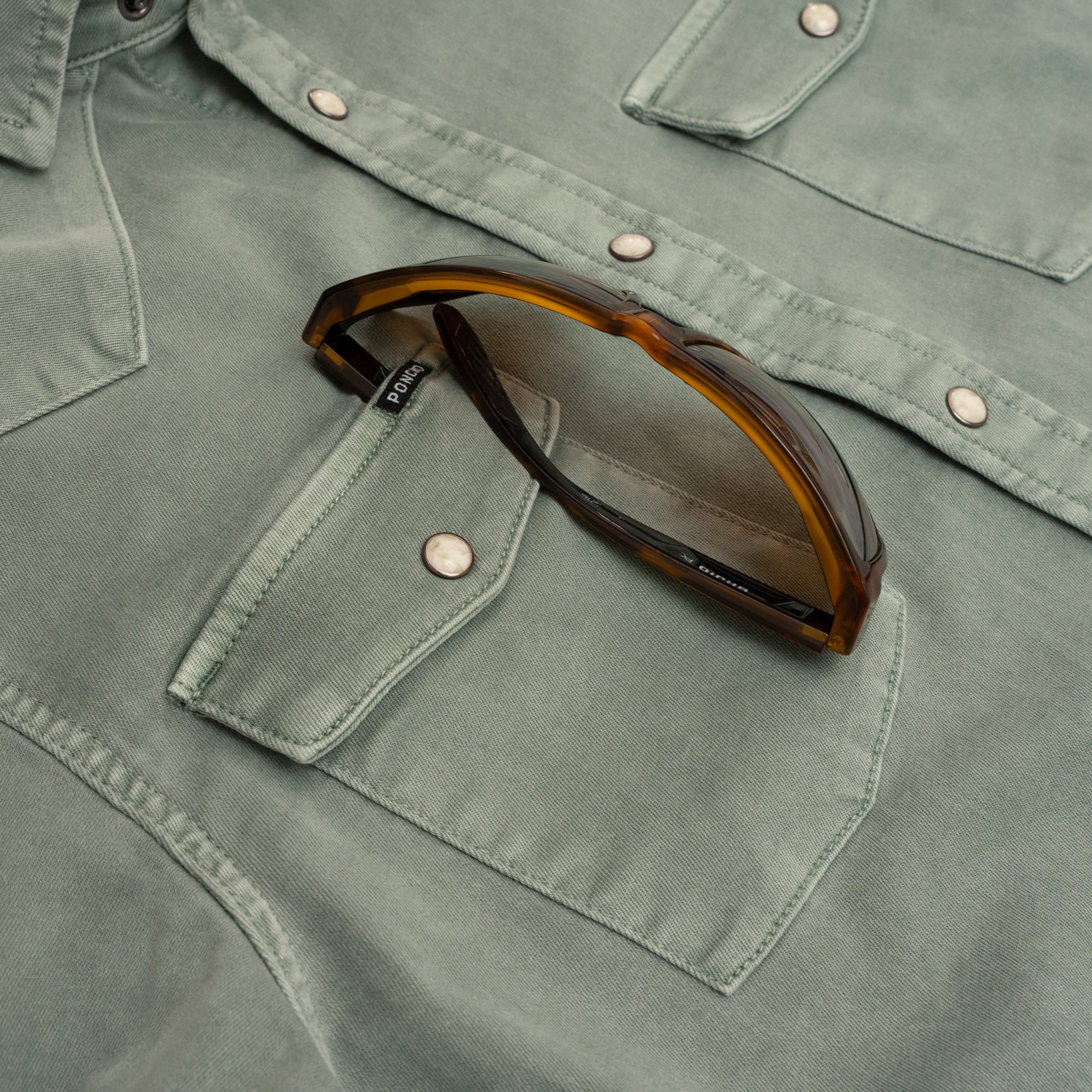 Sunglasses in pocket of green denim shirt