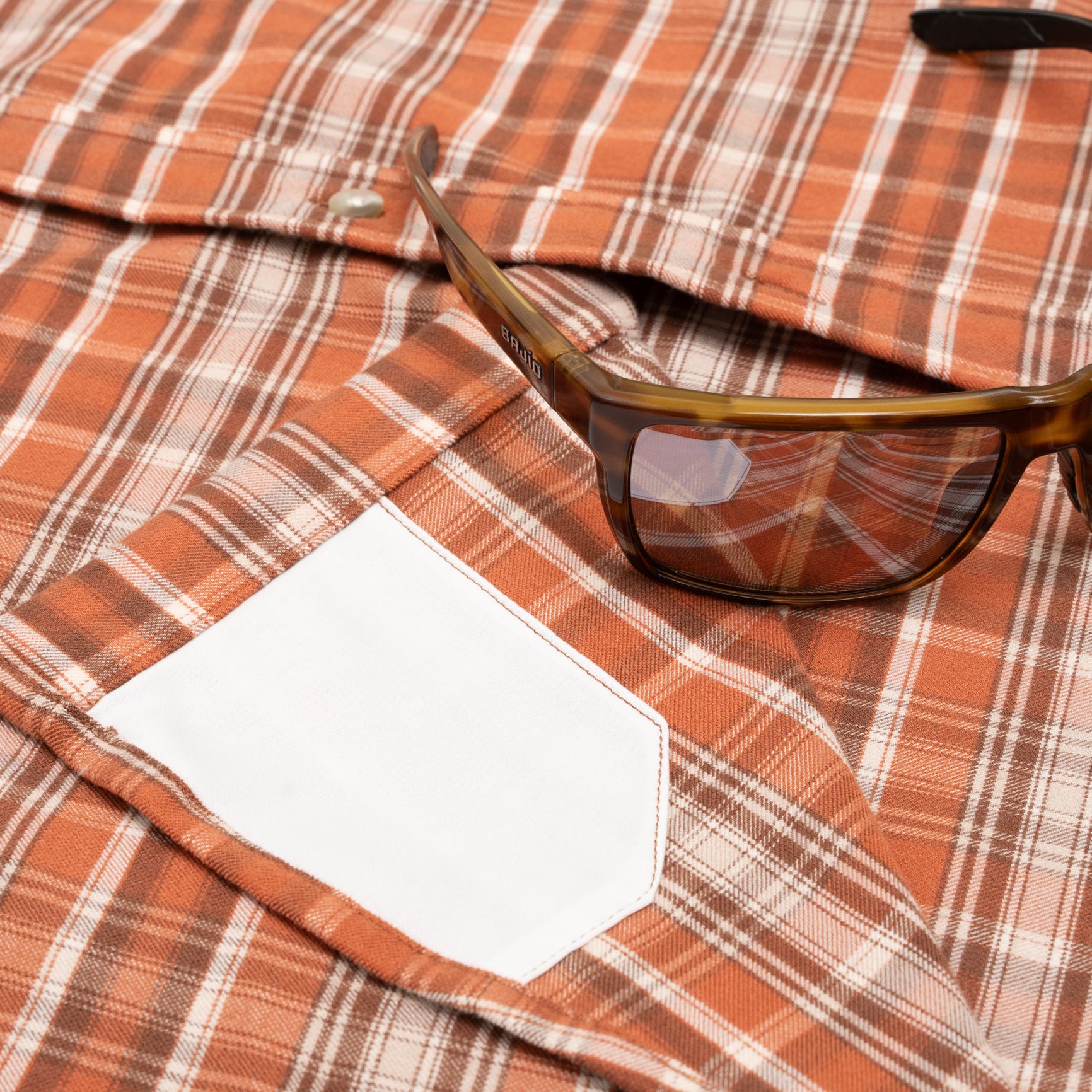 sunglasses next to sunglass hidden cloth fabric on orange plaid flannel