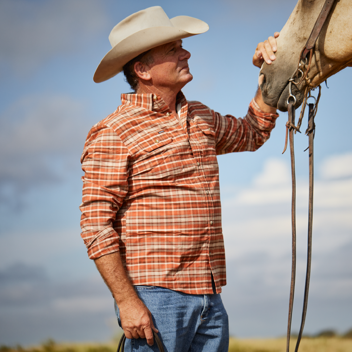 Man petting a horse while wearing an orange plaid flannel shirt