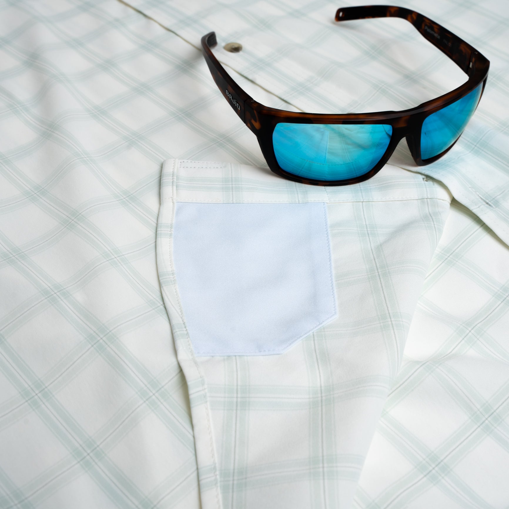 Close up of pocket of sunglasses laying on green button down shirt