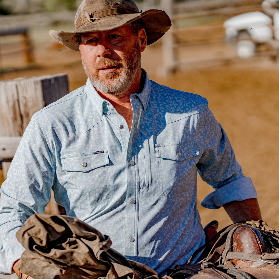 Man carrying a saddle while wearing the paisley blue western shirt