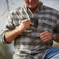 man putting his phone into the pocket of a black plaid flannel shirt