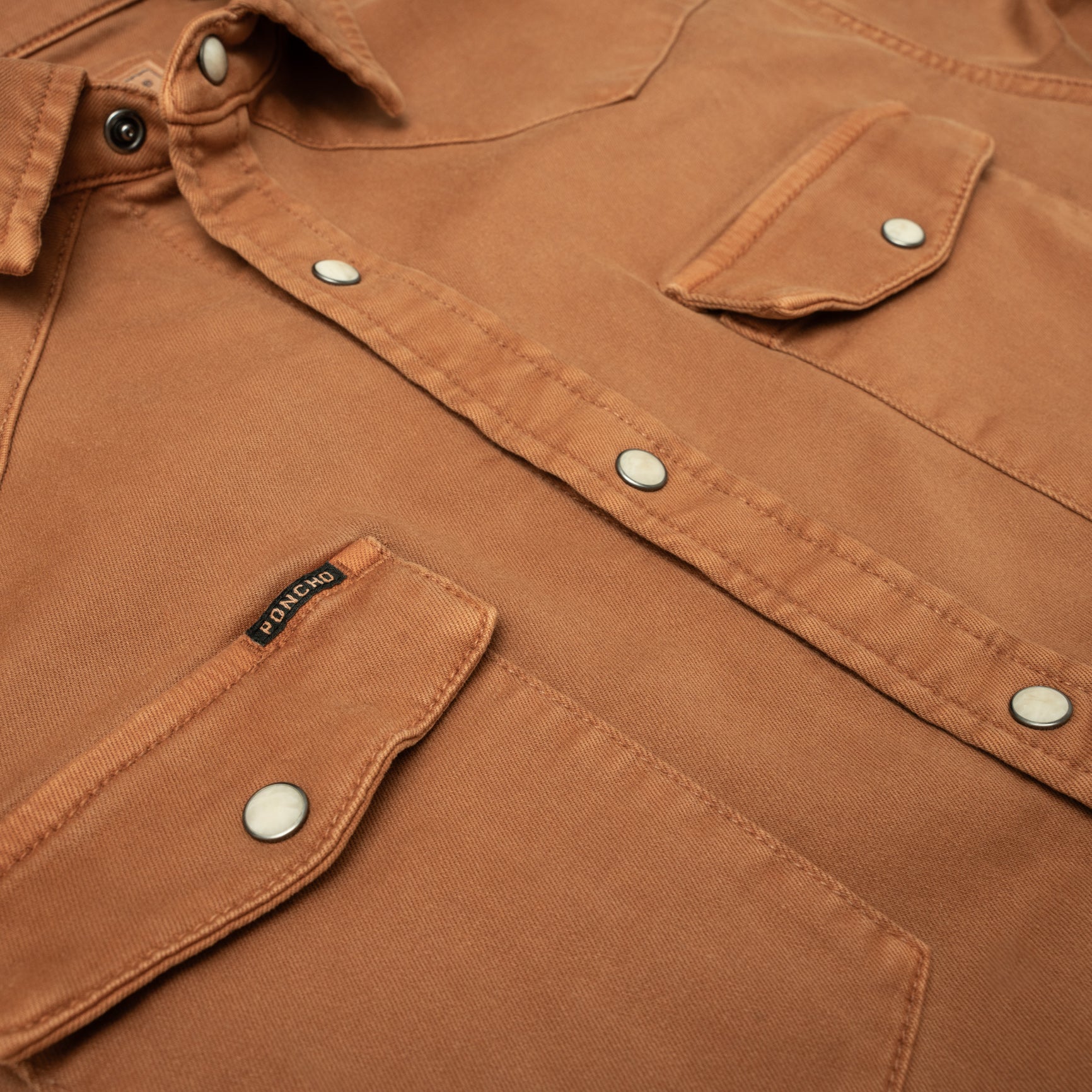 close up of burnt orange denim pearl snap pockets