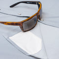 Close up of sunglasses with lens cloth on long sleeve blue striped shirt