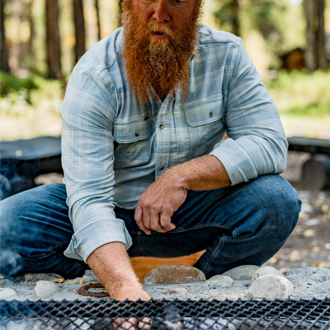 man lighting a fire while wearing a blue plaid flannel shirt