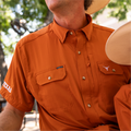 Photo of a man holding his child while wearing a burnt orange button down shirt