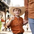 Young boy holding his dads hand at a football game wearing burnt orange short sleeve