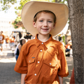 young boy in a cowboy hat while wearing the burnt orange western short sleeve