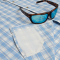 Sunglasses laying on a blue button down short sleeve shirt