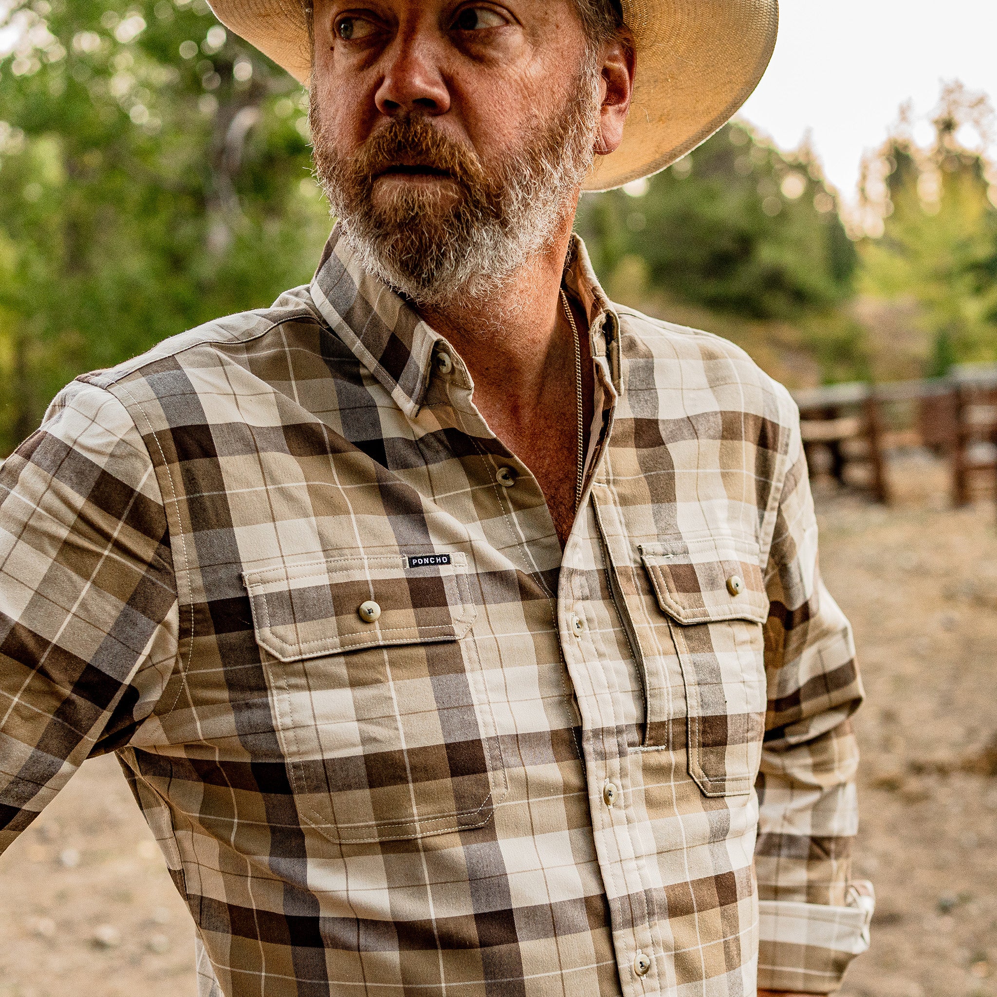 Man standing at a horse corral wearing the button down plaid flannel