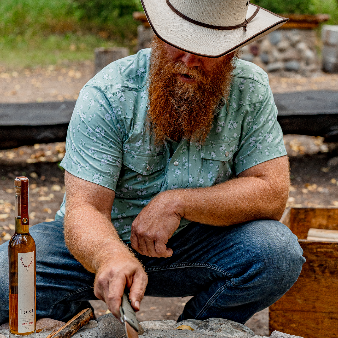 Close up photo of man wearing green shirt while tending a campfire