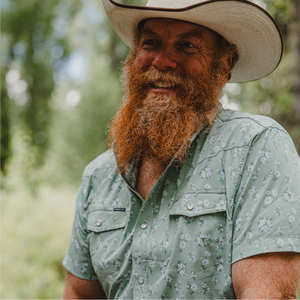 Cowboy wearing green floral short sleeve shirt in the woods