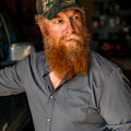 man leaning on truck wearing grey button down shirt